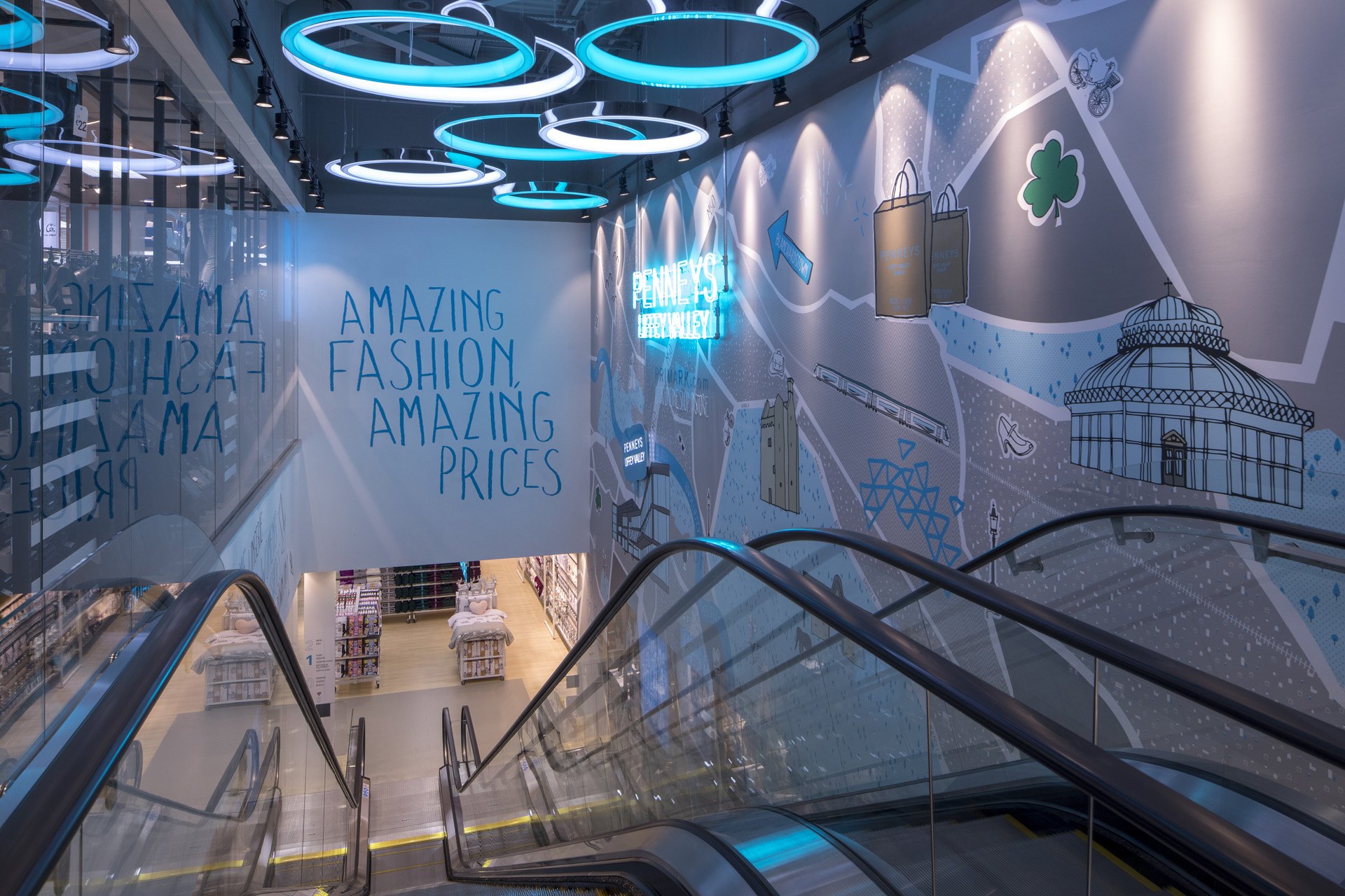 Escalators rising under a ceiling of large illuminated rings, with a lit graphics wall behind