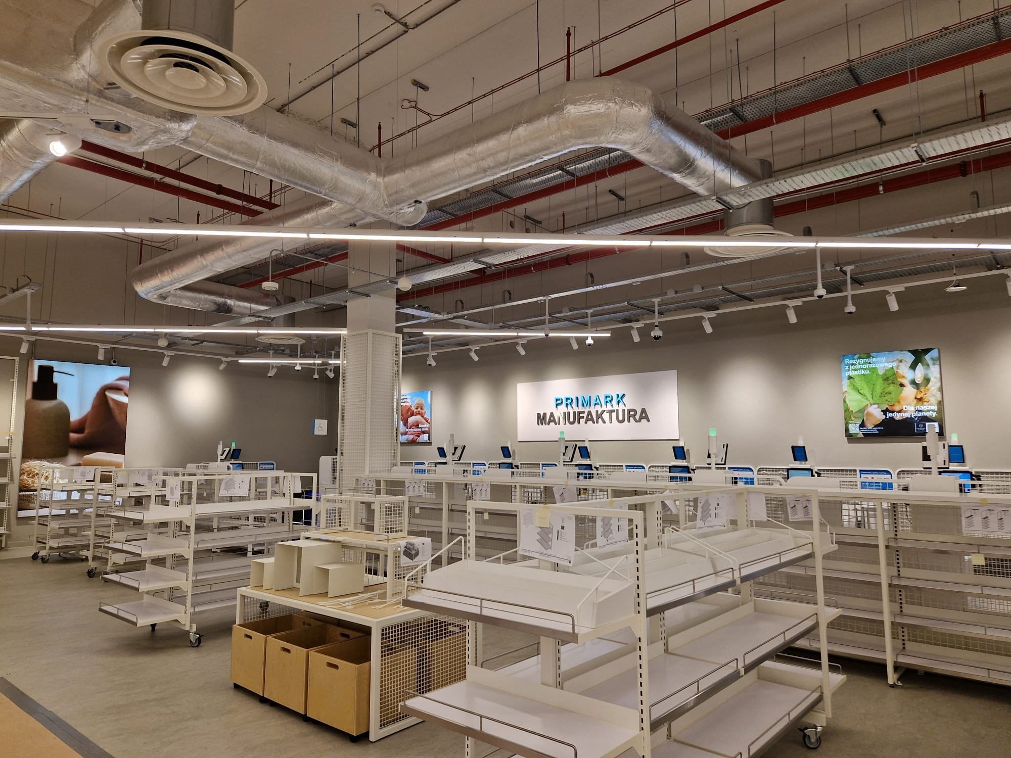 Shop floor before opening with the ceiling still open, showing ductwork, cable containment and track lighting